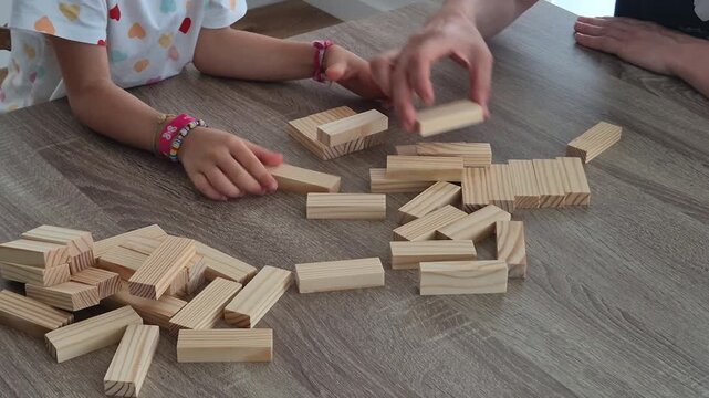Close-up of a family playing a wooden block tower game at home. Hands carefully stacking and removing blocks, highlighting concentration, balance, coordination, dexterity, and fun family bonding.
