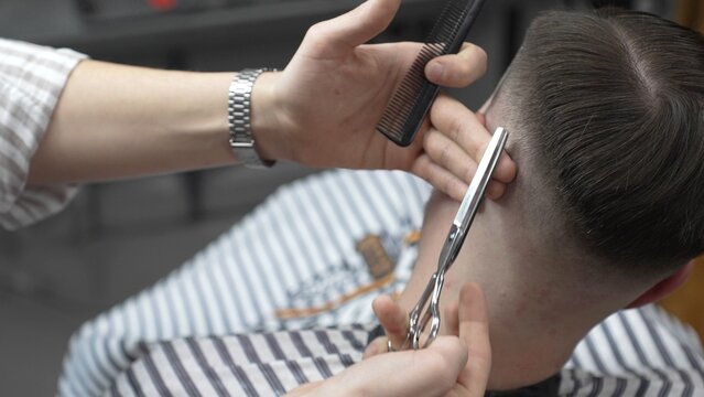 Professional barber cutting client's hair with scissors and comb, creating a stylish fade in a modern barbershop, providing a high quality grooming service