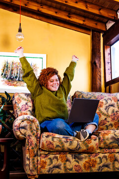 Happy woman celebrating success working remotely on laptop at home sofa