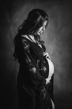 Ritratto di profilo in bianco e nero di una donna incinta in abito di pizzo nero che tocca la pancia