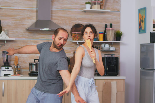 Carefree couple sings together in morning kitchen, linking breakfast, domestic routine and home comfort inside a domestic kitchen setting.