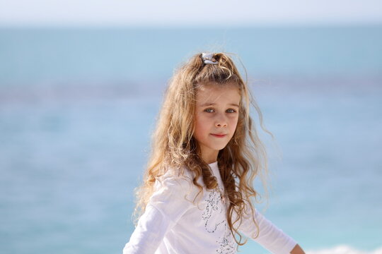 Ritratto a mezzo busto di una bambina bionda con maglia bianca davanti al mare blu
