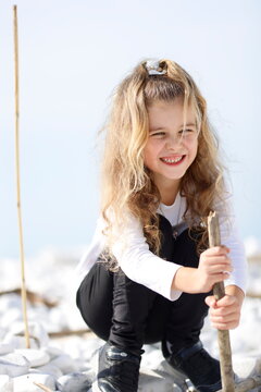 Bambina bionda sorridente che gioca all'aperto sulla spiaggia con un bastone di legno