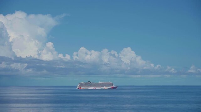 Norwegian Cruise, Caribbean Sea - APRIL 21, 2026: Massive white cruise liner with colorful hull art travels through tranquil turquoise waters beneath towering cumulus cloud formations on sunny day.