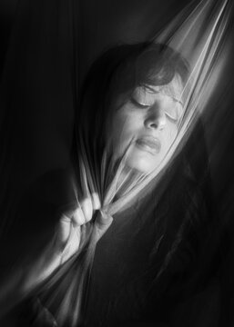 Ritratto artistico in bianco e nero di donna dietro telo trasparente che tiene stretto in una mano