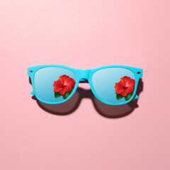 Naklejka premium Sunglasses with reflection of hibiscus flower under blue sky on pink background