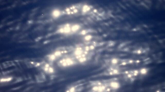 Abstract close-up of deep blue water surface with bright sunlight creating sparkling bokeh reflections. Gentle ripples and waves create mesmerizing patterns of light dancing across the tranquil water.
