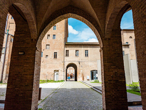 Castello dei Pio archways framing a stone courtyard with traditional brick buildings, high walls, and a view of the sky in Carpi, Emilia Romagna, Italy