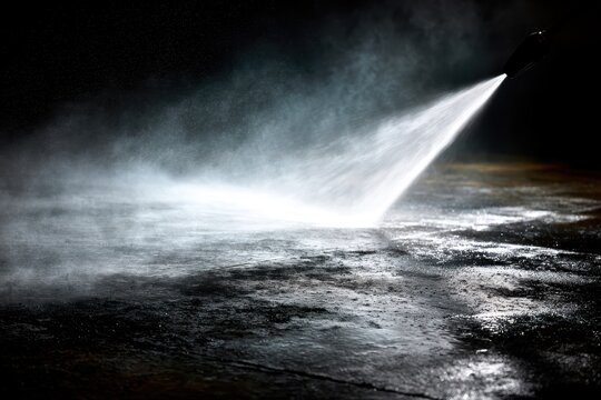 Highpressure water jet spraying onto a dark concrete surface, creating a mist and wet texture