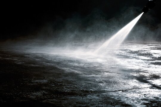 Highpressure water jet spraying onto a dark concrete surface, creating a mist and wet texture