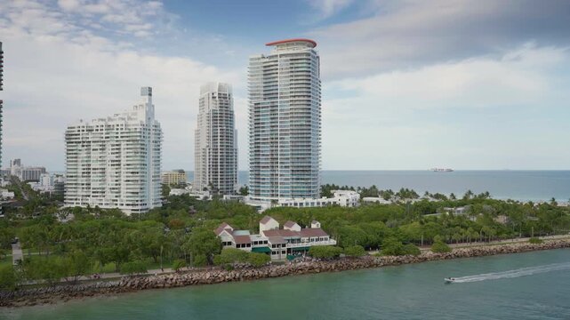 Port Miami waterfront aerial view on April 21, 2026 showcasing South Beach luxury high-rise condominiums with tropical palm trees along rocky shoreline and turquoise waters with speedboat passing by.