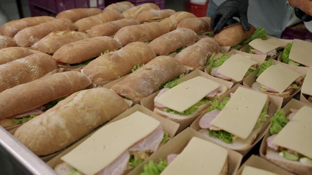Freshly prepared sandwiches with layers of lettuce, ham, and cheese being assembled in a commercial kitchen, showcasing the process of sandwich making in a food production setting