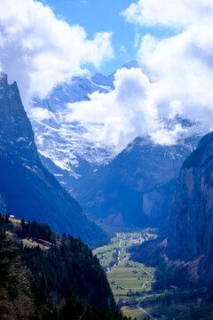 A breathtaking, vertical landscape photograph showcasing the dramatic u-shaped Lauterbrunnen Valley nestled deep between massive limestone cliffs in the Bernese Oberland region. Captured from an eleva