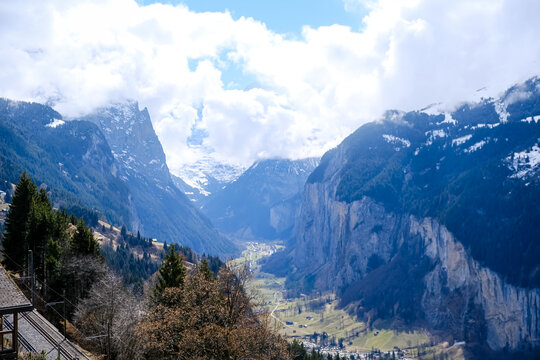 A breathtaking, vertical landscape photograph showcasing the dramatic u-shaped Lauterbrunnen Valley nestled deep between massive limestone cliffs in the Bernese Oberland region. Captured from an eleva