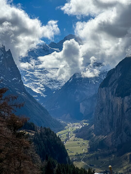 A breathtaking, vertical landscape photograph showcasing the dramatic u-shaped Lauterbrunnen Valley nestled deep between massive limestone cliffs in the Bernese Oberland region. Captured from an eleva