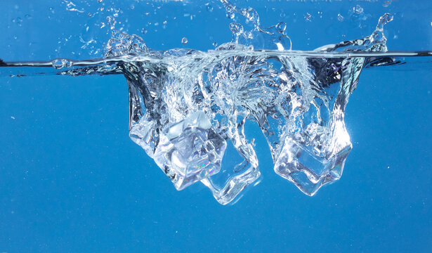 Falling ice cubes in motion with splashing water, creating air bubbles scatter around, blue background isolated. Ice cubes fall into water with air bubbles