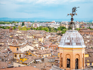 Obraz premium Bell tower dome with an angel weather vane overlooking the historic city center of Modena, Italy, showcasing traditional terracotta tiled rooftops under a clear sky