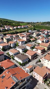 Vertical aerial drone view of Roseto degli Abruzzi town residential houses near green vineyards and scenic hills under blue sky in Abruzzo region Italy.