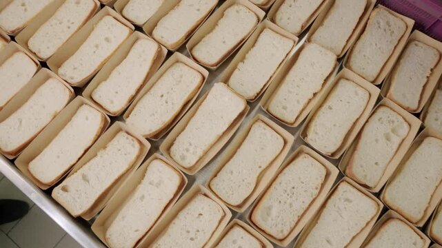 Freshly sliced white bread loaves arranged neatly in trays, showcasing a consistent pattern of packaging and presentation in a commercial kitchen setting