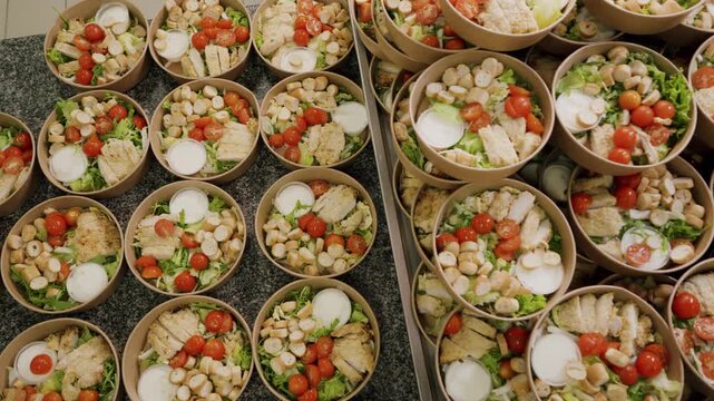 Multiple bowls of fresh salad with chicken, cherry tomatoes, croutons, and dressing arranged on a countertop in a commercial kitchen setting for meal preparation