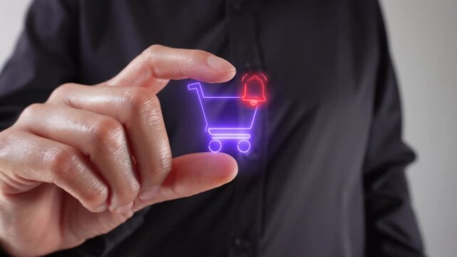 Close-up of a hand holding a glowing shopping cart icon with a notification bell. It suggests an online purchase or e-commerce action.