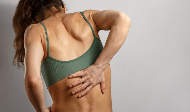 Woman holding painful lower back with one hand in pain problem. Concept of lumbar pain, backache, muscle strain, physiotherapy, rehabilitation, healthcare and chronic pain	
