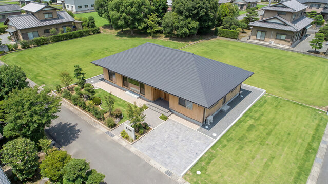 灰色の寄棟屋根を持つ平屋住宅と広い芝生の庭を上空から見た航空写真