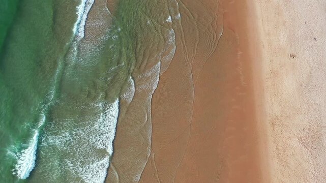 Waves flow onto the sandy beach while the tide moves in during bright daytime hours aerial view. Water glistens as it washes ashore and recedes quietly.