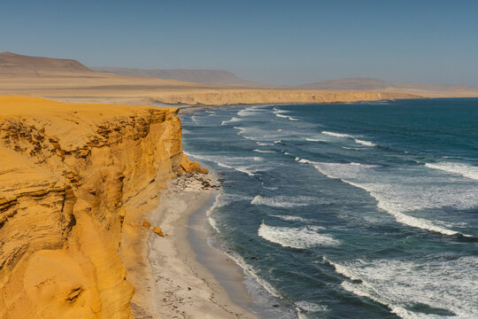 Golden sandstone cliffs overlooking breaking Pacific Ocean waves along the rugged desert coastline of Paracas National Reserve, Peru