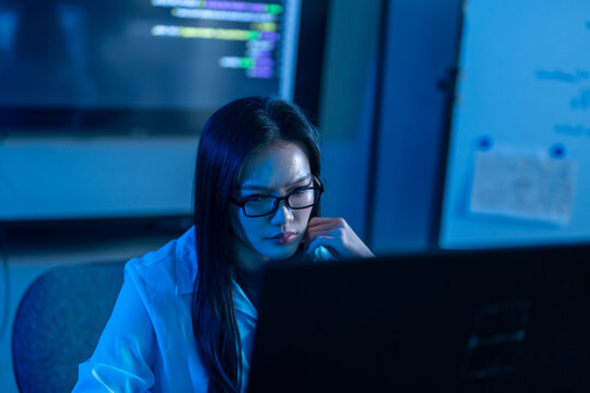 Asian female programmer coding on computer in dark office, Woman software developer typing code late at night, IT cyber security engineer working with male colleague, Tech data center hacker concepts