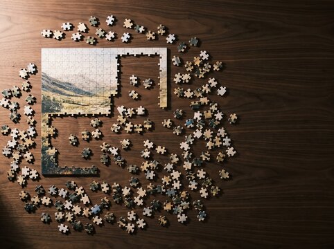 Partially assembled landscape jigsaw puzzle with scattered pieces on wood