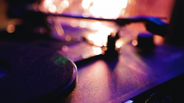 Person playing vinyl record on turntable. Close up of needle dropping on rotating disk. Music concept with retro audio equipment, vibrant lights and analog sound.