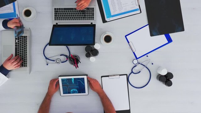 Doctors check x ray records beside stethoscope and digital devices during a medical conference, arranged as an overhead clinical workspace with copy space.