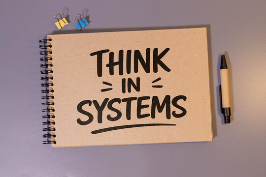 Think in Systems Motivation on Kraft Notebook Cover in Minimal Office Workspace.