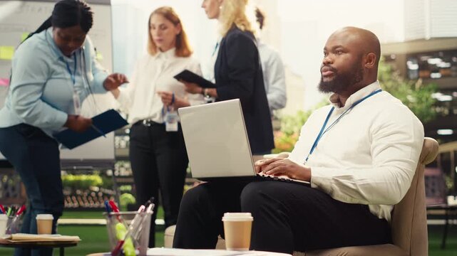 Seated businessman working on laptop during outdoor work session, notes on pc with city buildings and business park downtown, business casual productivity, for business planning.