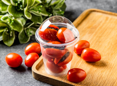 Fresh cherry tomatoes in a plastic cup. Healthy snack food served on a wooden board.