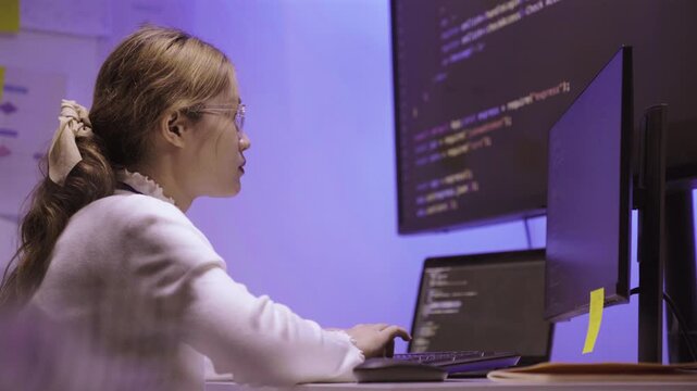 Female software developer writing code on computer screen in office