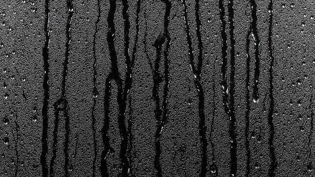 Realistic rain water drops dripping down a glass surface for video overlay and blending effects in high contrast.