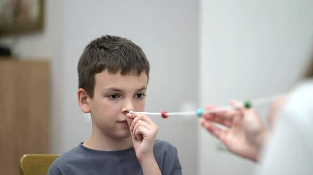 Mother helps her young son practice a vision therapy exercise with a colorful beaded string to improve eye coordination and focus at home.