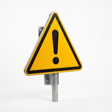 Warning Sign Alert: A bright yellow triangular warning sign with a black border and an exclamation mark inside, mounted on a metal pole, stands as a symbol of caution.