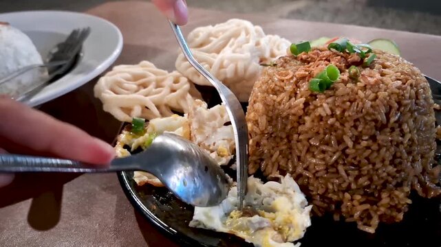 Close-up shot of authentic Indonesian fried rice (Nasi Goreng) served with fried egg, green onions, and traditional white kerupuk crackers on a black plate.