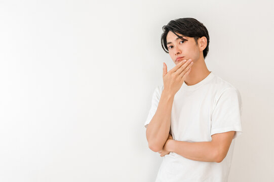 A young Asian man resting his chin on his hand (dissatisfied, worried, troubled, troubled, anxious, imagining)