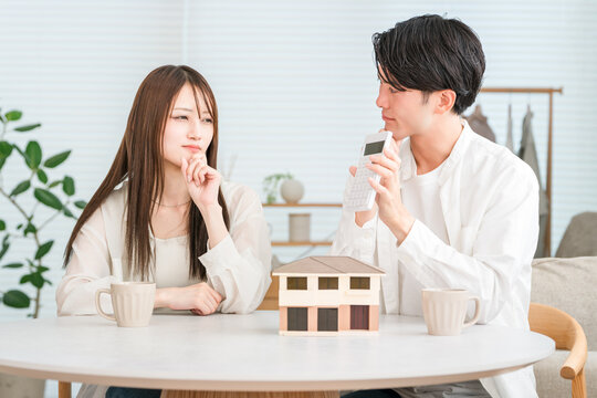 A young Asian couple discusses their budget for their dream home while looking at a model house.