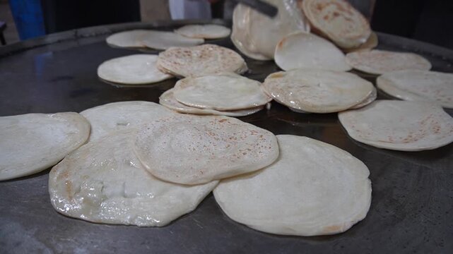 Fresh round flatbreads or parathas stacked neatly on a large hot metal griddle in a commercial street food kitchen