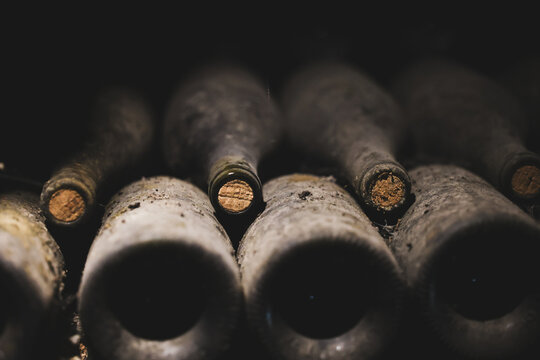 Close‑up view of vintage wine bottles resting in a dark, dusty cellar. Aged bottles and corks stored for preservation. 