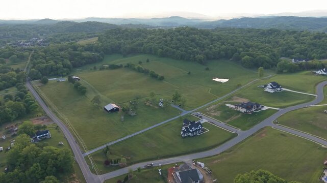 Aerial perspective of a suburban area in Johnson City, Tennessee, highlighting green hills, residential houses, winding roads, and expansive fields bathed in soft morning light