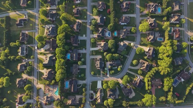 Aerial perspective of a suburban area in Johnson City, Tennessee, featuring various residential houses, lush green lawns, swimming pools, and curving roads illuminated by sunlight on a clear day