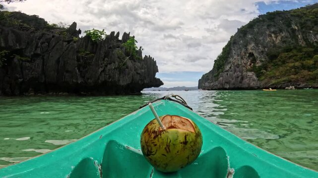 Coconut drink placed on a kayak in clear turquoise water, with rocky cliffs and lush greenery creating a stunning tropical landscape
