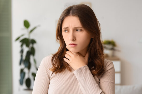 Young woman experiencing a sore throat or neck pain, health and medical discomfort concept, feeling unwell indoors
