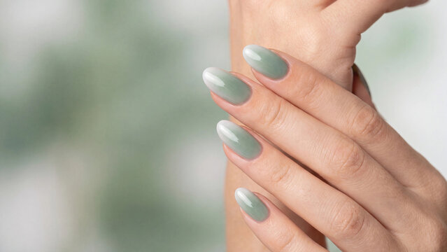 Hands held together reveal a sophisticated sage green ombre gradient polish on long oval nails with a soft blurred interior background providing ample space.